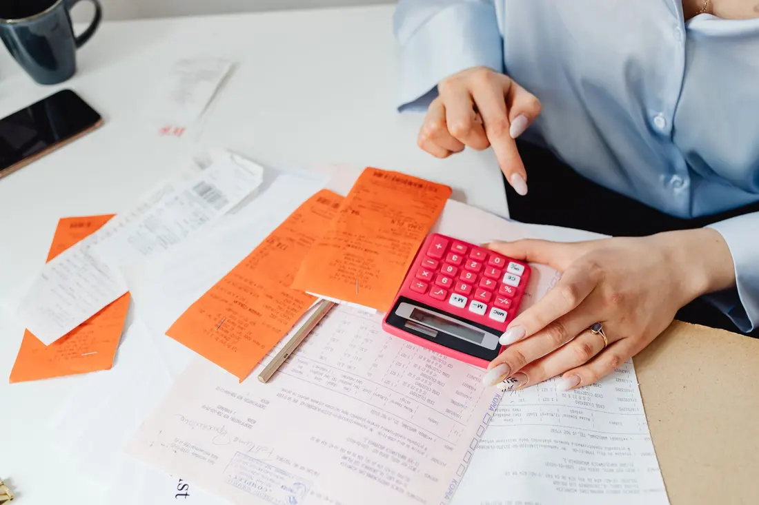 Hands using a calculator next to receipts and handwritten notes on a desk