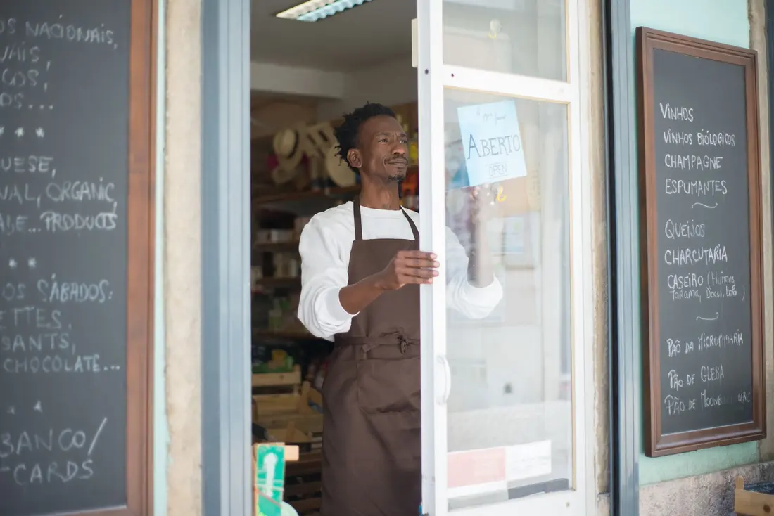 A shop owner standing in the doorway of his store beside chalkboard menus