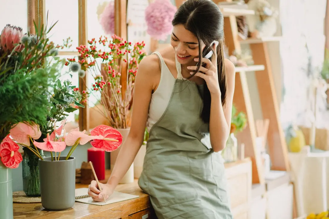 A florist in her shop taking a phone call and writing the details in a notebook