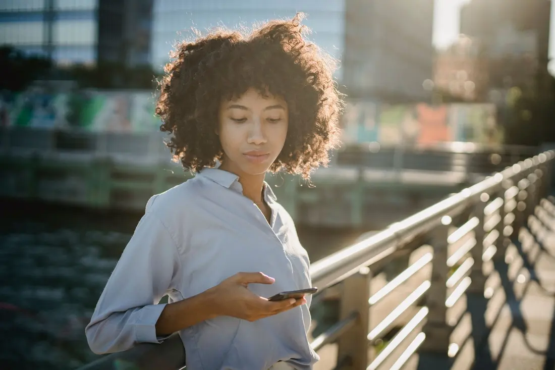 A woman standing outside on a city walkway looking at her phone, mid search
