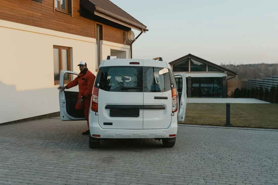 A tradesman loading tools into a work van parked on a house driveway