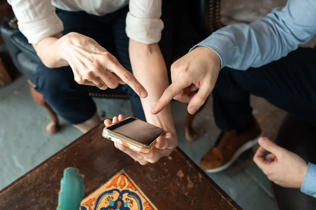 Two people leaning over a phone together, one pointing at the screen